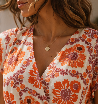 Detalhe do tecido leve e plissado do vestido, com estampado floral coral, laranja e ameixa sobre fundo off-white