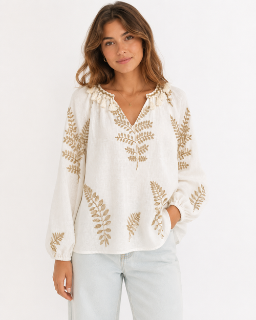 Modelo a usar blusa cru com bordado dourado de folhas e pompons na gola, corte solto