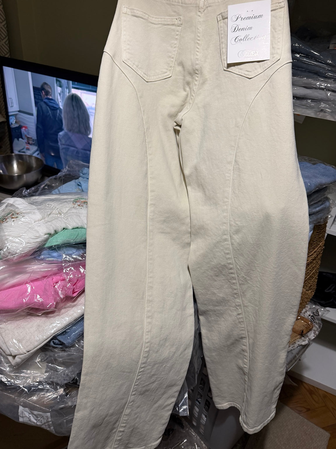 Pormenor real do bolso: tachas redondas prateadas no contorno do bolso e na costura curva das calças bege-creme