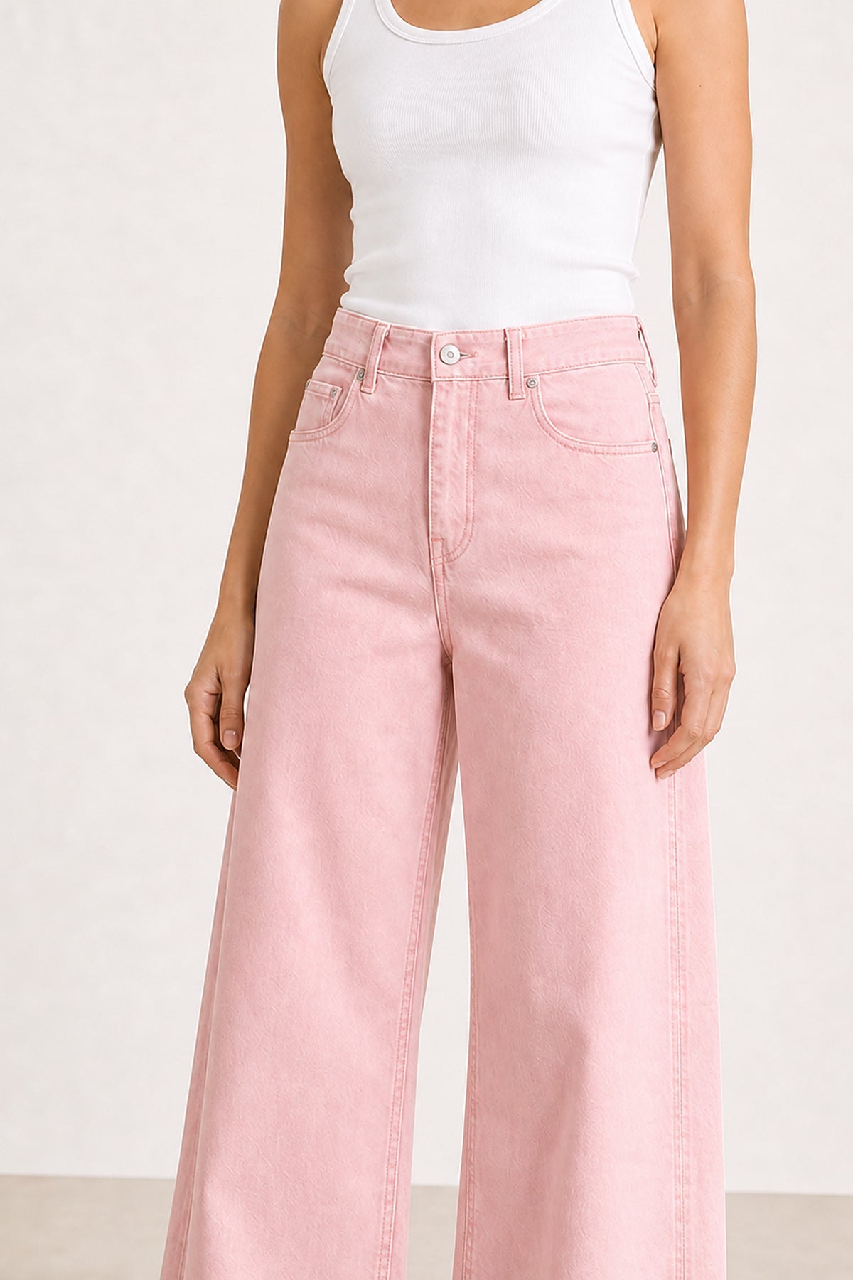 Detalhe do cós subido, botão, fecho e bolsos das calças em ganga rosa pastel